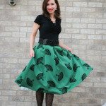 Lindsey wearing a black shirt with green midi fan skirt, black polka dot tights and black and white heels