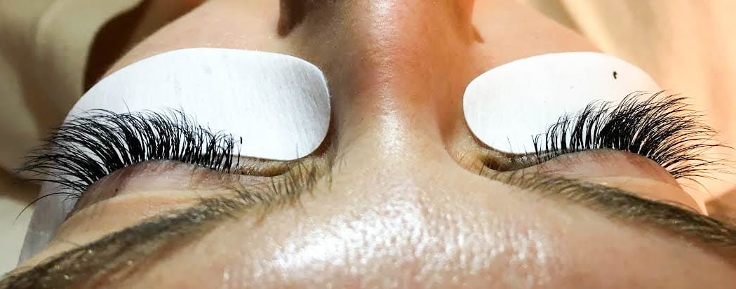 A closeup image of a woman's eyelashes after a lash extension procedure. She has long, wispy lashes on both eyes.