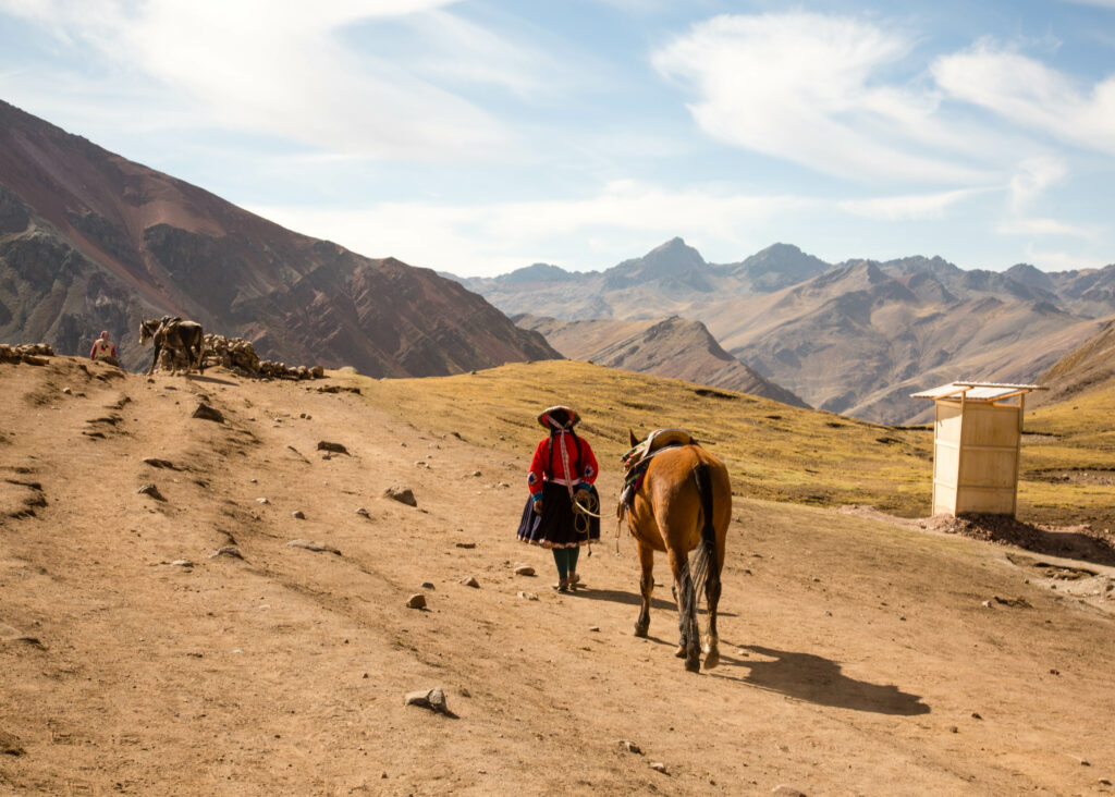 A woman walking a horse on a dirt path on the Rainbow mountains in Peru.