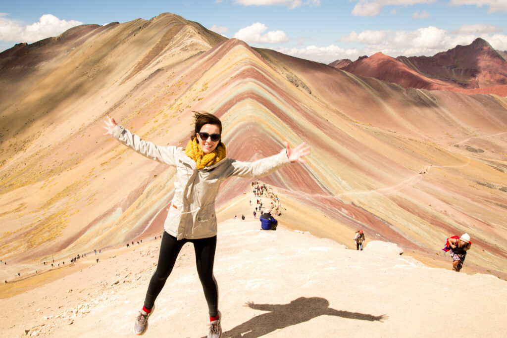 A woman standing on top of a rainbow mountain.