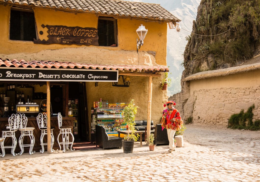 A man is standing in front of a lovely coffee shop in Ollantaytambo.