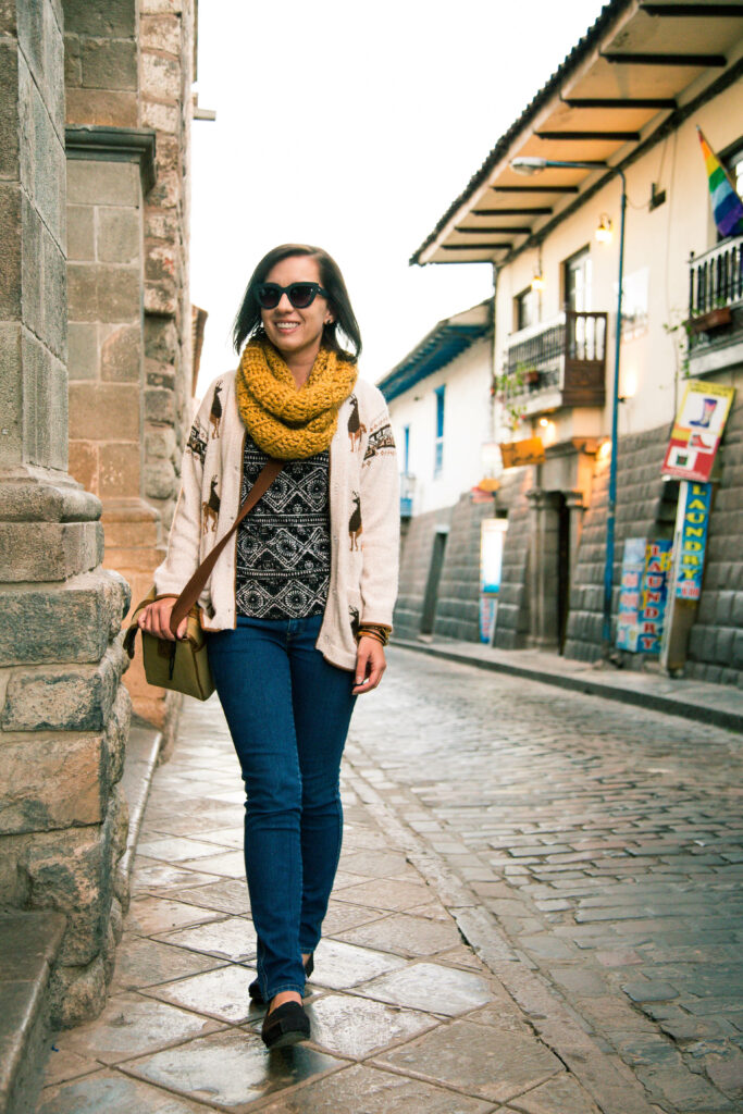 A woman walking down a cobblestone street in peru wearing an Alpaca sweater.