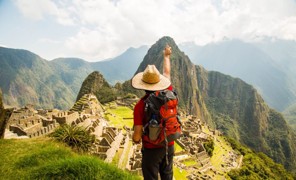 A man with an outstretched arm overlooking Machu Picchu. 