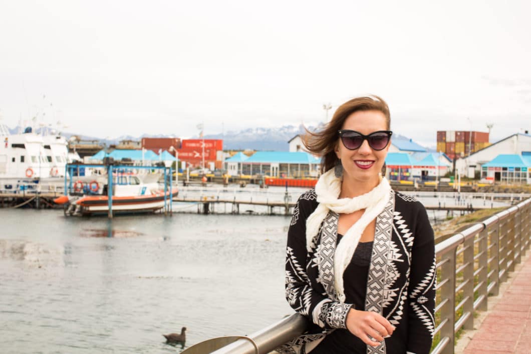 A woman is standing on a railing in front of the harbor in Ushuaia, Argentina.