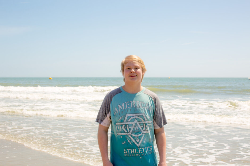 A teenage boy with blonde hair smiling in a blue shirt on the beach in Myrtle Beach South Carolina