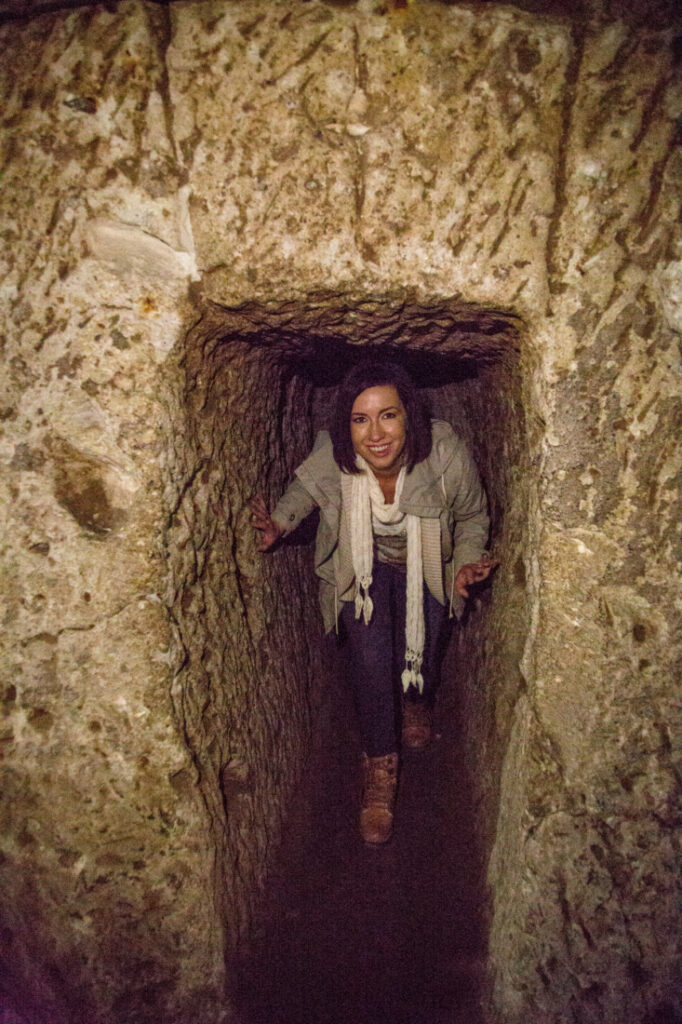 A woman smiling, crawling through a tunnel in Derinkuyu Underground City