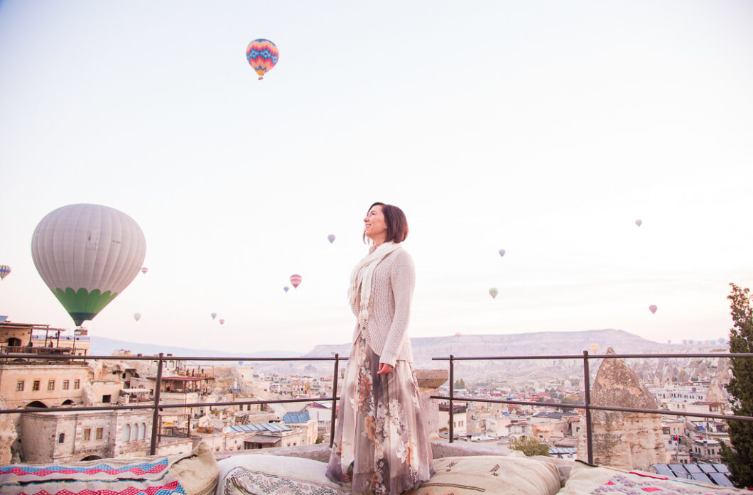 A woman wearing a floral maxi skirt, smiling as she looks up at the hot air balloons in Cappadocia, Turkey