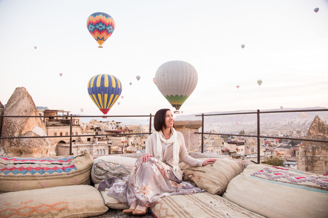 A woman sitting on a couch with hot air balloons in the background.