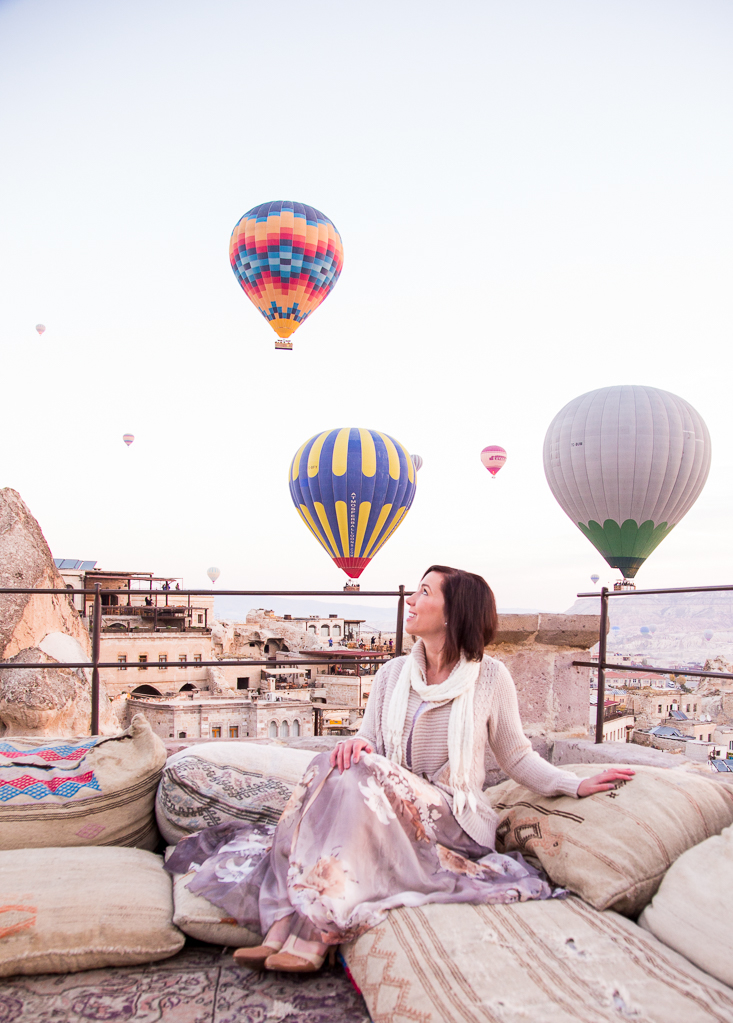 A woman sitting with hot air balloons in the sky.