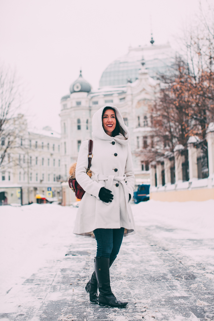 Lindsey of Have Clothes, Will Travel wearing a white hooded Steve Madden coat with black button, mittens, and boots. She is standing on a snowy sidewalk in Moscow Russia