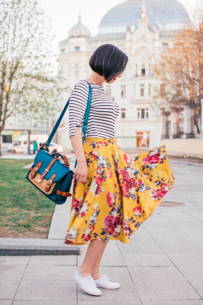 Lindsay poses outdoors in Moscow, Russia, wearing a knee-length yellow floral skirt and striped top.