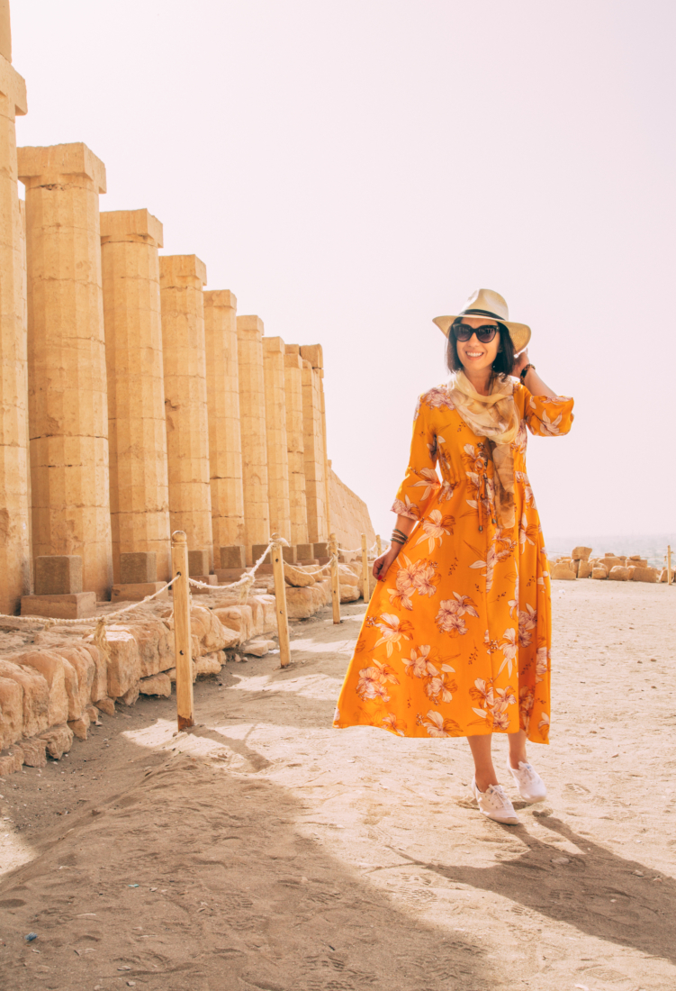 A woman in an yellow floral dress standing in front of pillars in the Valley of the Kings, Egypt.