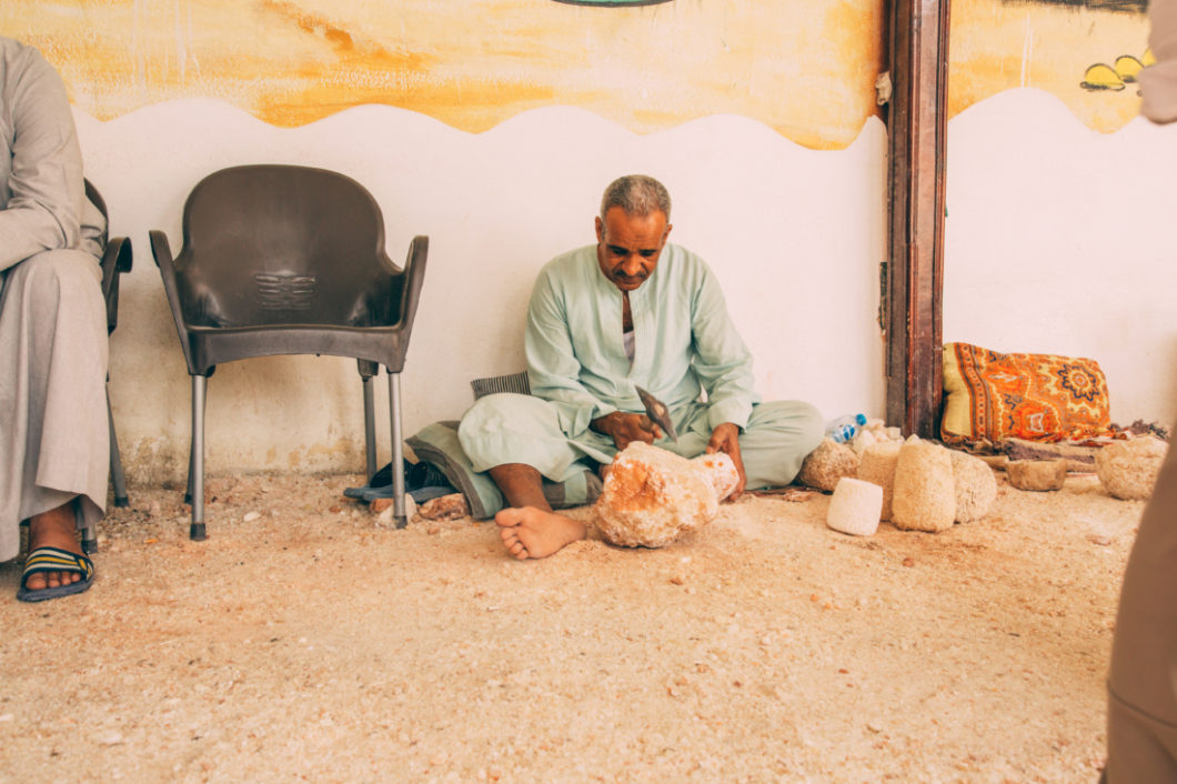 An Egyptian man sitting on the ground and carving a large piece of alabaster. 