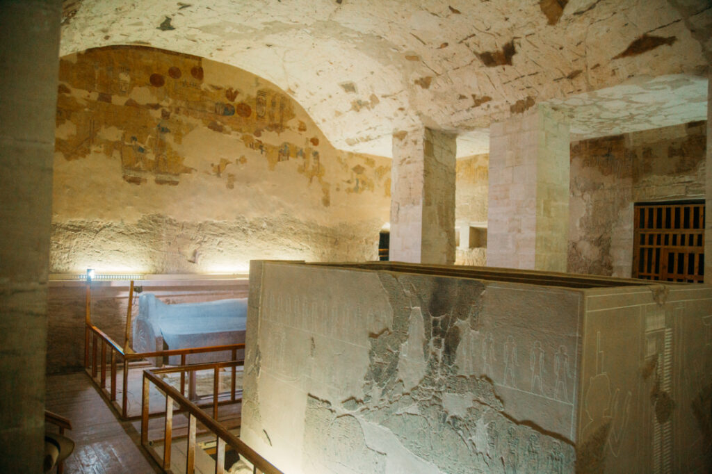 Inside a burial chamber in an Egyptian tomb. The sarcophagus and pedestal are protected by a wooden railing, and the room is Illuminated with spotlights.