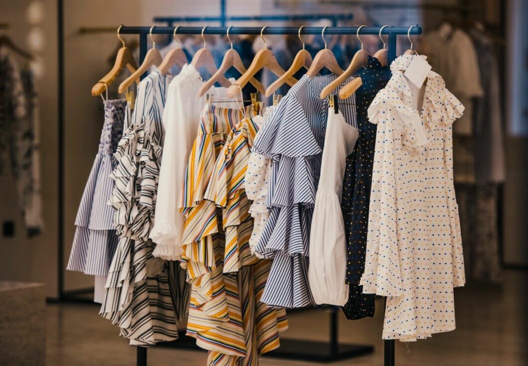 Blouses, skirts, and tank tops on wooden hangers hanging from a black hanging rod