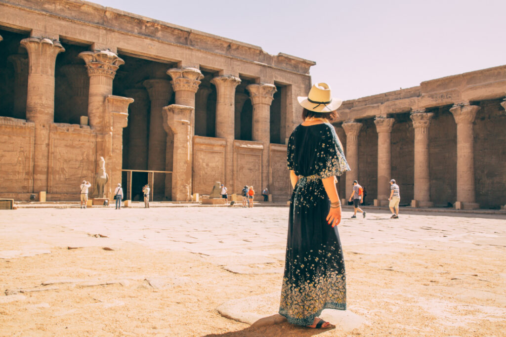 A woman in a maxi dress and hat standing in the courtyard of the Temple of Horus at Edfu