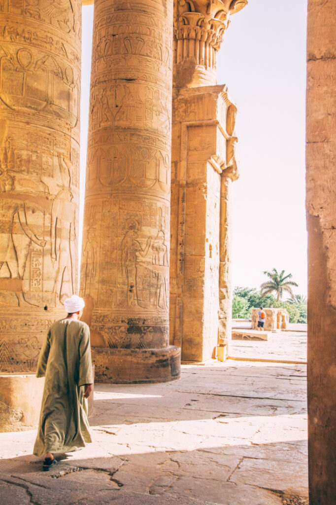 Giant columns in the Temple of Kom Ombo, with an Egyptian man walking past it in local clothes. 