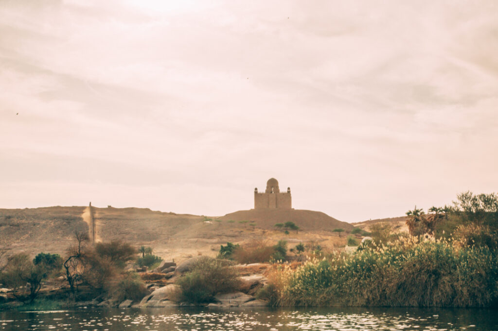 An image of the desert landscape near the Nubian Village in Aswan. Clear skies and bright sun over sandy hills and desert vegetation.