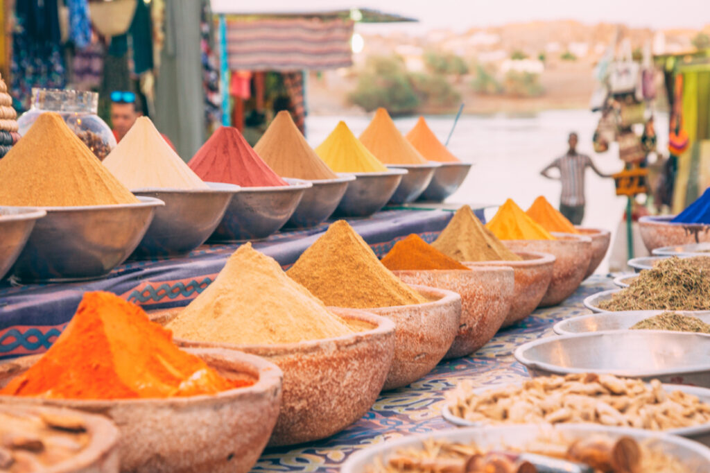 Rows of bowls filled with spices and herbs line the shelves of a street vendor stall in the Nubian Village