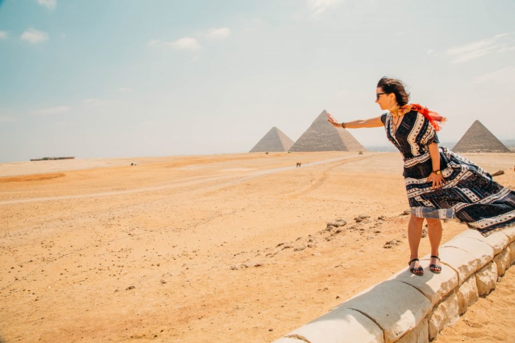 A woman is standing in front of the pyramids of Giza in a flowy maxi dress.