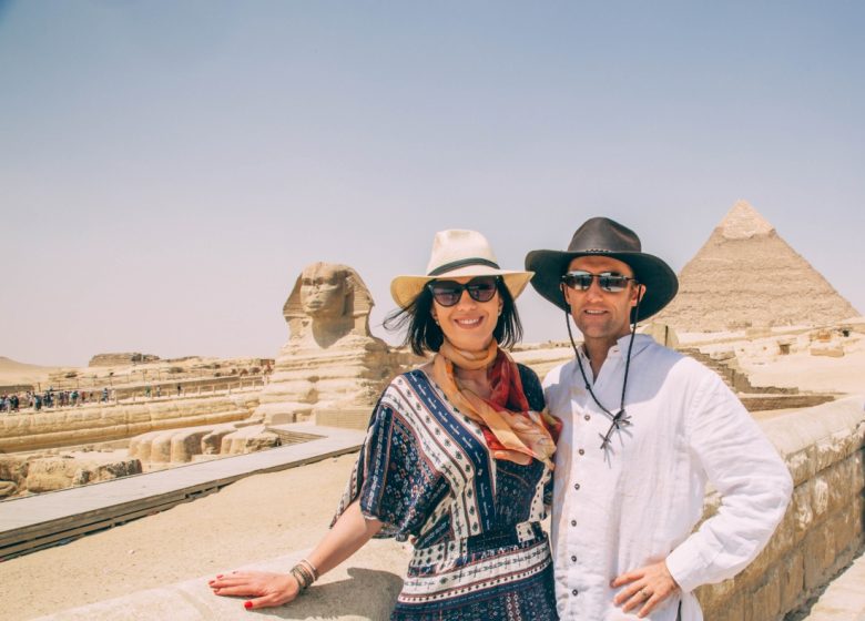 A couple smiling and posing with the Sphinx and Great Pyramid of Giza in the background.