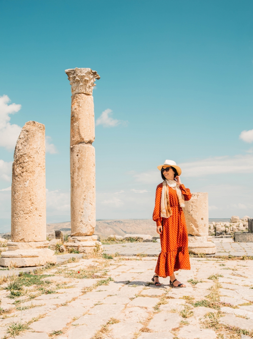 Woman wearing a polka dot maxi dress walking past ancient columns in Jordan