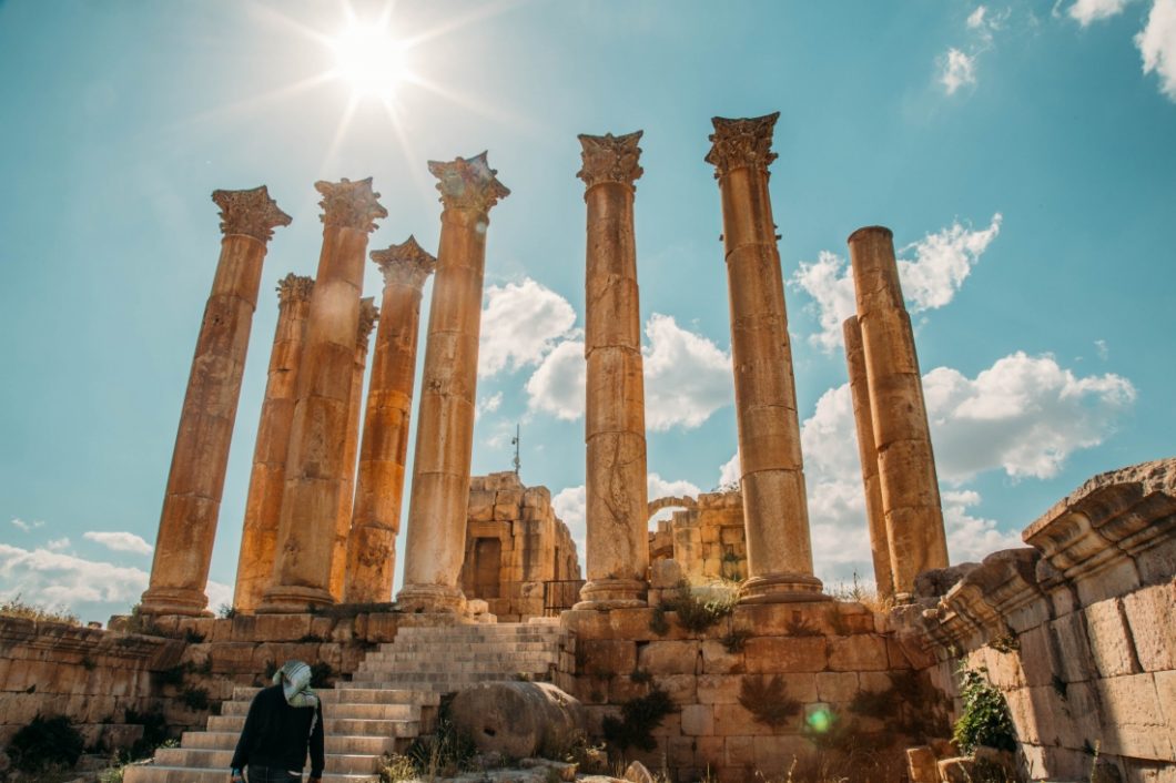 A woman is standing in front of a group of ancient pillars in the sun in Jordan.