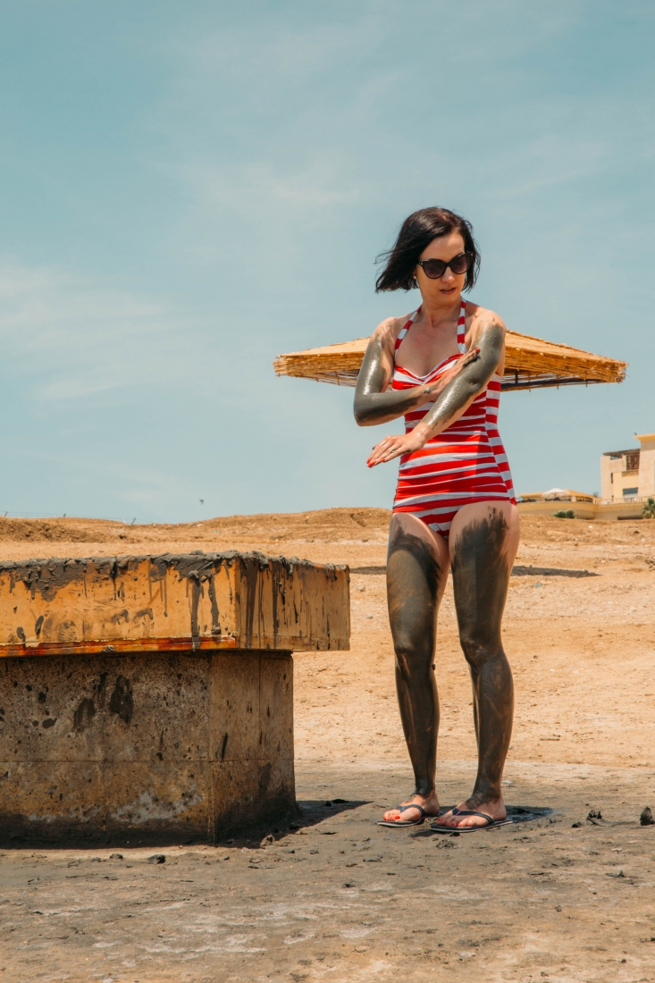 A woman in a striped swimsuit slathering dead sea mud on herself.