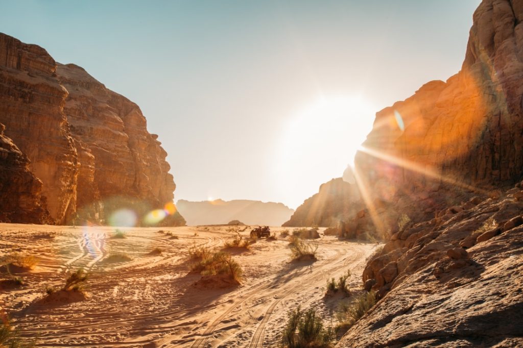 The sun shines between towering rock formations on either side of a narrow valley in the Wadi Rum desert.