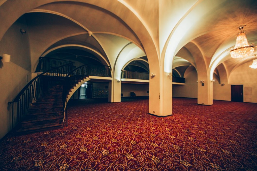 A large empty room with arched ceilings and patterned carpet, and a staircase. This room is where the wine cellar would have been in the book A Gentleman in Moscow.