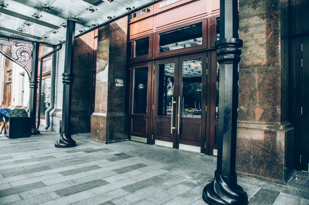 The main entrance to the Metropol hotel features large brown wooden doors under a glass canopy covering the sidewalk in Moscow, Russia.