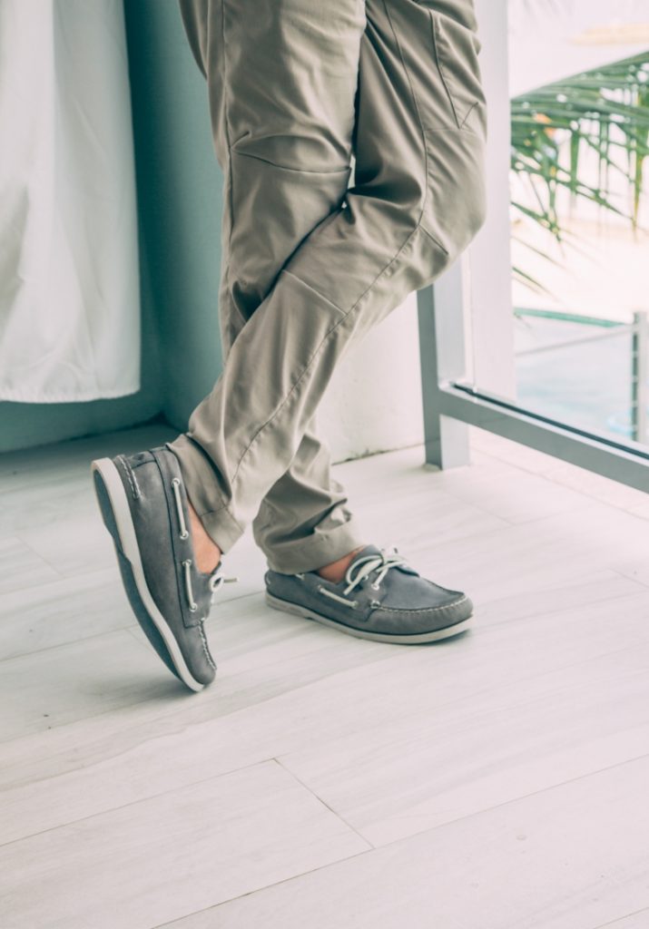 A man in gray pants wearing sandals and standing next to a window.