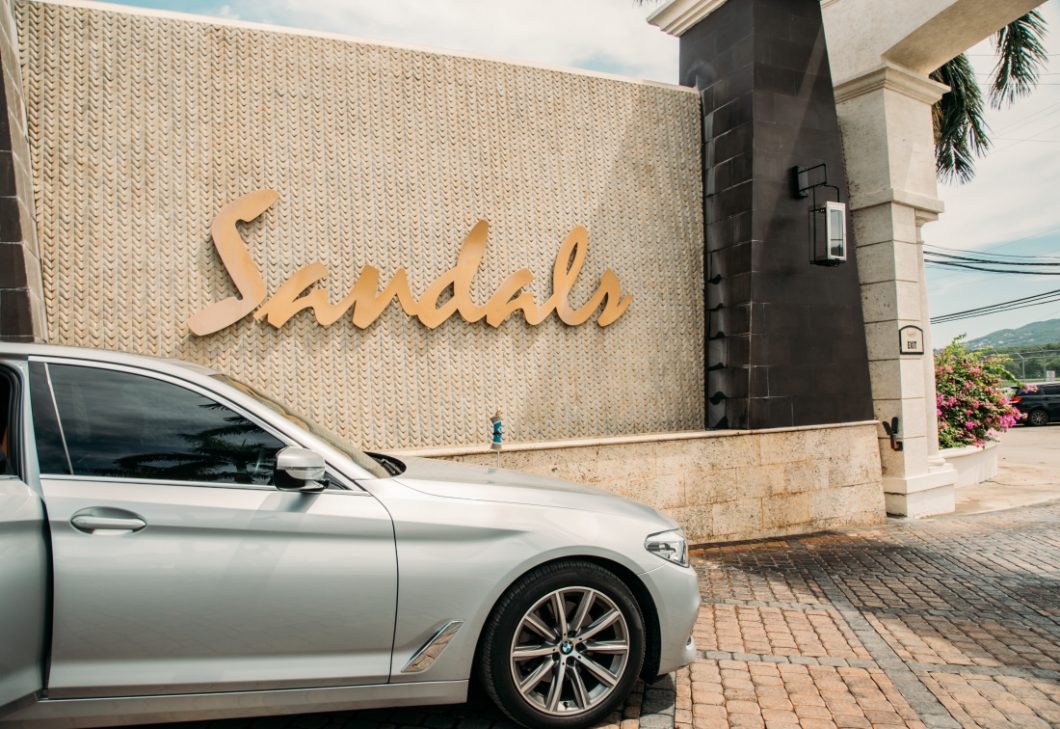 The Sandals sign with a silver BMW parked in front of it.