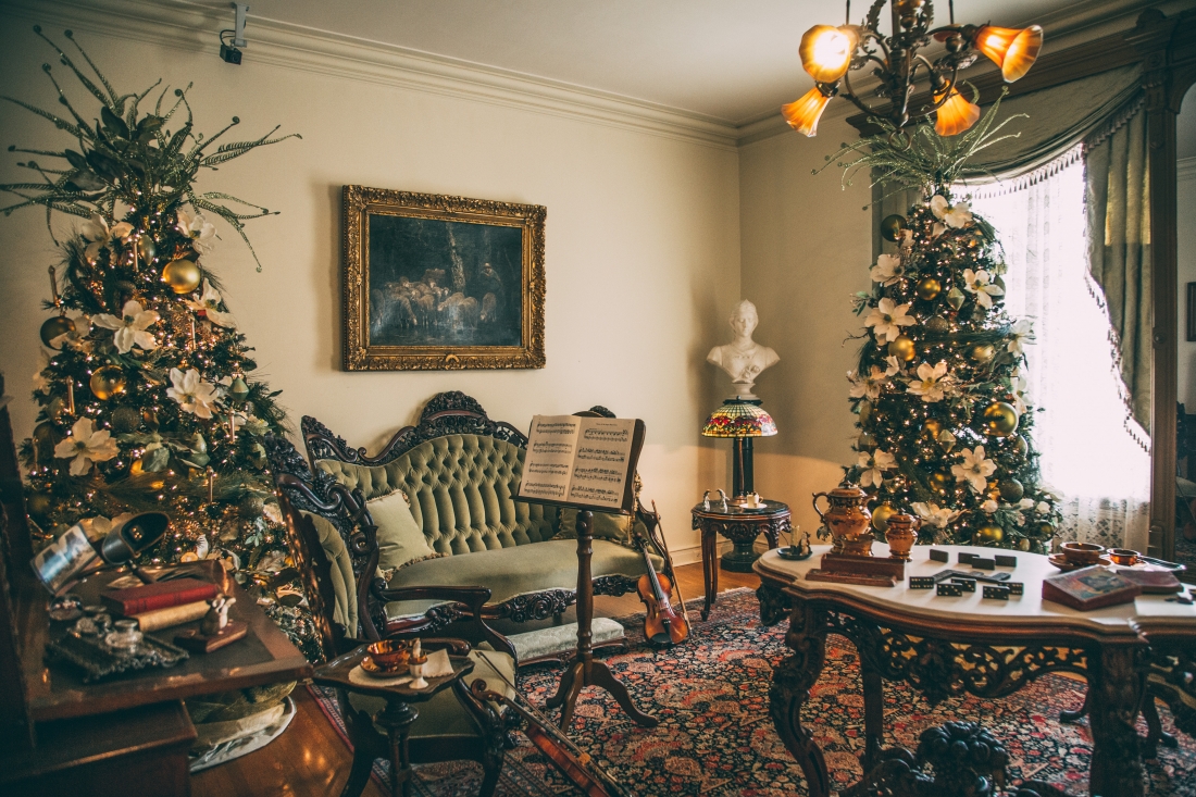 Another elegant sitting room filled with antique furniture and two large decorated Christmas trees. Sheet music rests on a music stand, next to a chair with a violin propped up next to it.