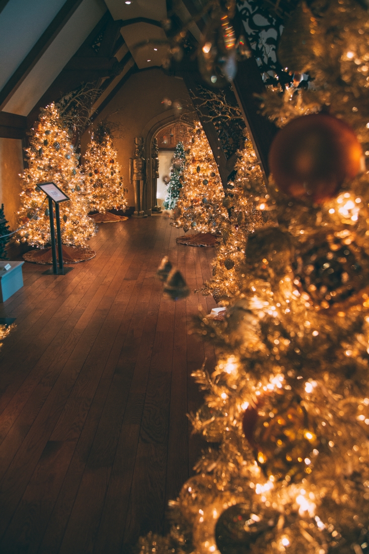 A large room is filled with brightly lit Christmas trees. Nutcracker statues stand on either side of the entrance to the room.