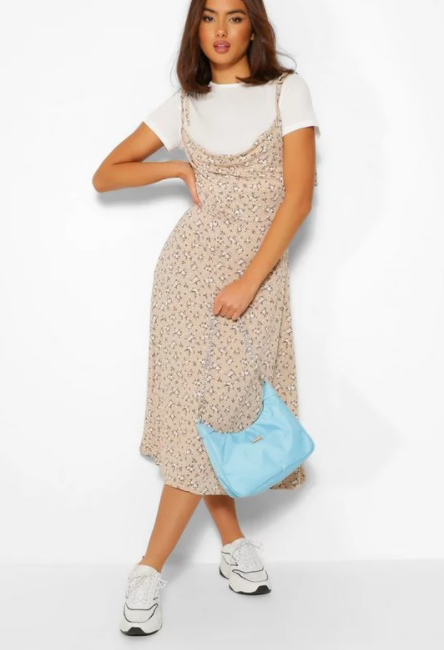 A woman wearing Short Sleeve T-Shirt & Ditsy Floral Midi Slip Dress by boohoo with a white t shirt underneath and sneakers. She is holding a blue handbag against a white wall.