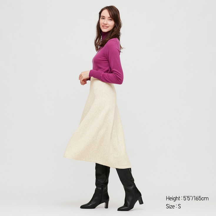 A woman wearing a pink sweater with a cream WOMEN SOUFFLE YARN FLARE SKIRT and black boots by Uniqlo