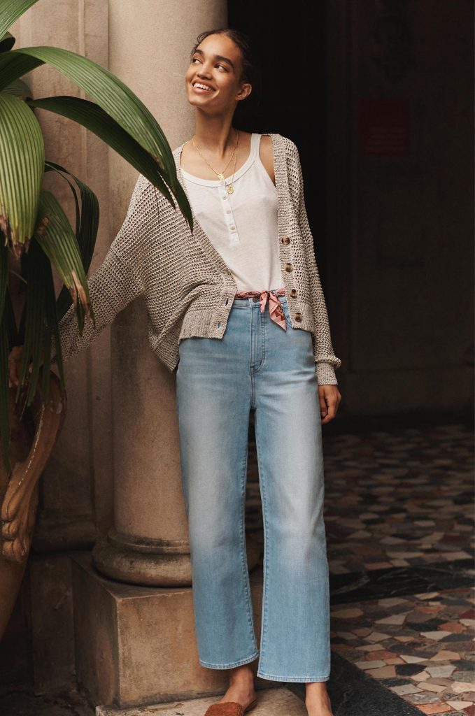 A woman wearing wide leg madewell jeans, and a white tank top with a cardigan over it.