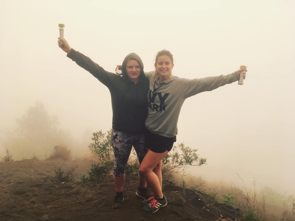 Two people pose on a cliff in front of a thick, foggy background that is completely obscuring the Mount Batur in Bali, Indonesia.