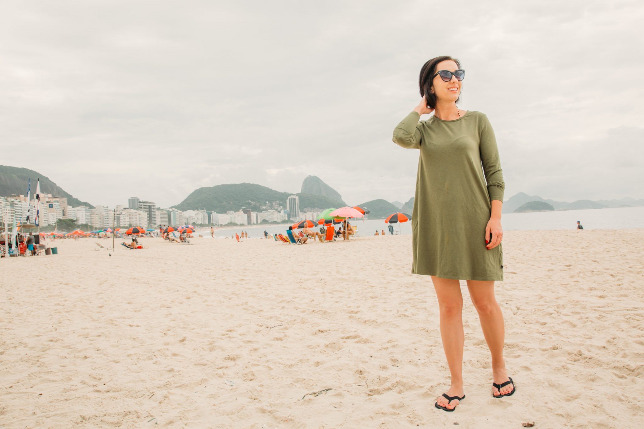 A woman poses on a beach wearing an olive-green long-sleeve dress from sustainable clothing brand United By Blue.