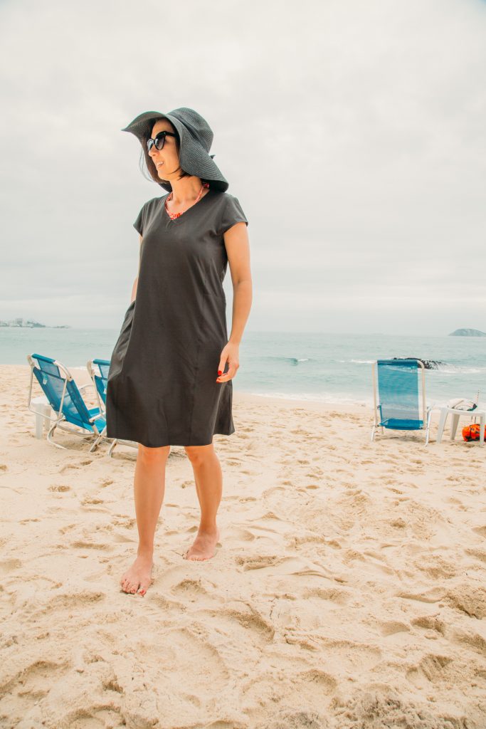 A woman wearing a black coverup and hat on the beach. 