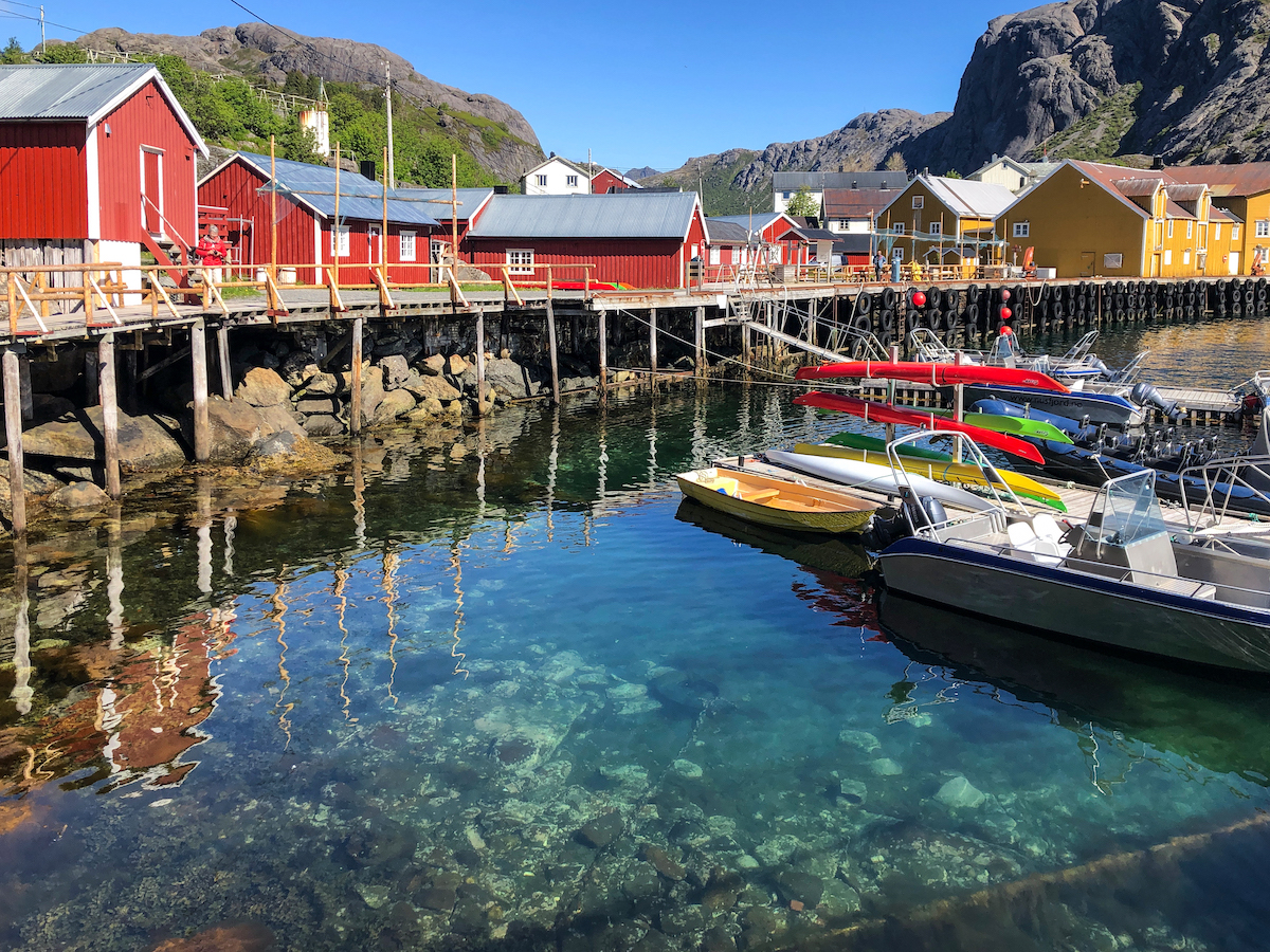 Nusfjord Arctic Resort featuring red barn like building on stilts over the water, and a variety of boats tied to the dock