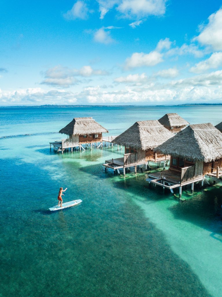 A person paddle boarding toward the overwater bungalows at Azul Paradise, Panama