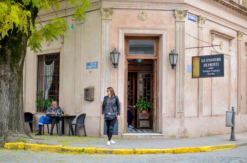 A woman stand on the street in front of a Parilla in San Antonio de Areco