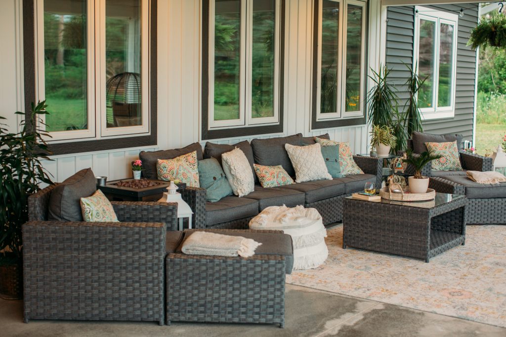 A 9-piece outdoor sofa set features a four-seat sofa, two chairs with ottomans, side tables, and a large coffee table. The set is a charcoal gray color and decorated with colorful outdoor pillows.