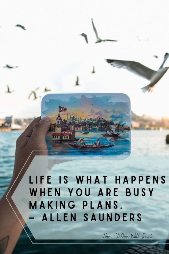 A person holds a watercolor postcard up in front of it's pictured scene - a waterfront marina where seagulls are flying in the sky. Text across the image reads, Life is what happens when you are busy making plans. - Allen Saunders"