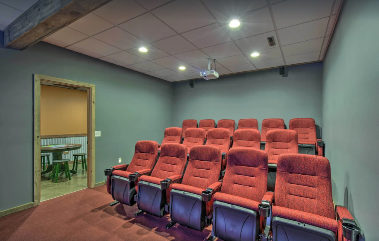 A private indoor move theater has three rows of movie theater style seats facing a large projector screen wall.