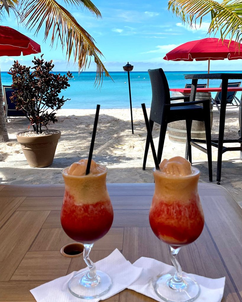 Two smoothies on a table with bright blue sea in the back.