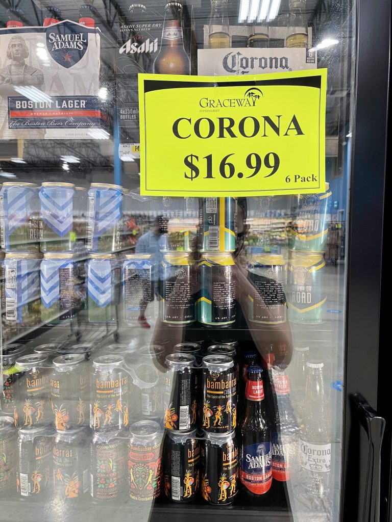 A sign on a grocery store refrigerator reading Corona $16.99 for 6 pack in Turks and Caicos.