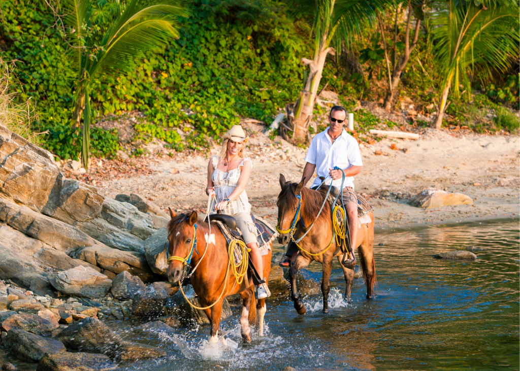 A man and woman riding horses on a beach.